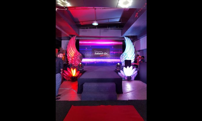 Empty stage set with illuminated angel-wing decor flanking a screen that reads "Sabash Q4".