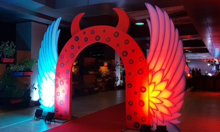 Illuminated red arch with devil-horn and wing motifs marking a red-carpet entrance at night, matching the wing decor style of the Sabash Q4 stage.