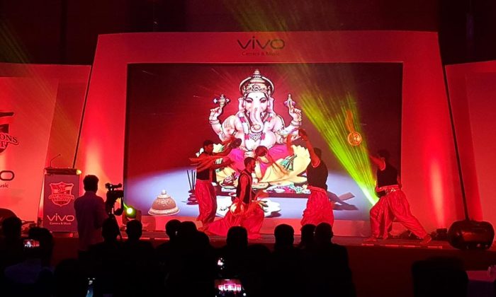 Dancers performing in front of a Ganesh graphic on a "Vivo Camera & Music" branded stage backdrop, red lighting.