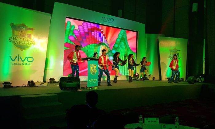 Dance troupe in sequined costumes performing on a green-lit "Vivo Champions Night" stage with a colorful LED backdrop.