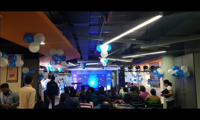 Office corridor decorated with hanging blue and white balloons, staff gathered for an indoor celebration near a blue LED backdrop stage.