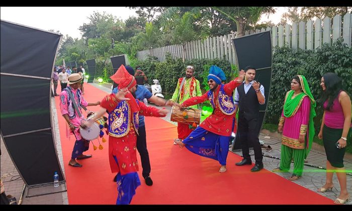 Additional view of the same Bhangra dancers and drummers performing on the outdoor red-carpet walkway.