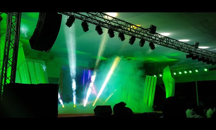 Empty stage under a marquee/tent ceiling lit in green with stage haze, moments around a performance.