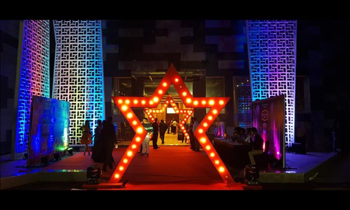 Illuminated red star-shaped entrance archway in a hotel lobby with patterned wall panels lit in blue and purple.