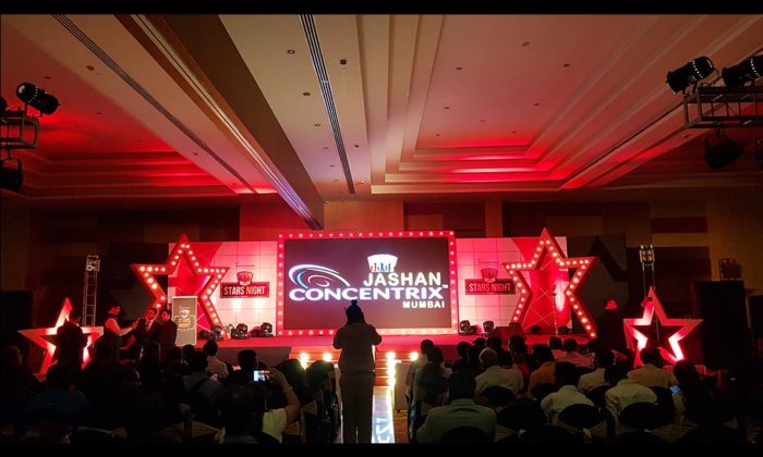 Indoor ballroom stage reading "Jashan Concentrix Mumbai - Stars Night" flanked by large lit red stars, seated audience facing the stage.