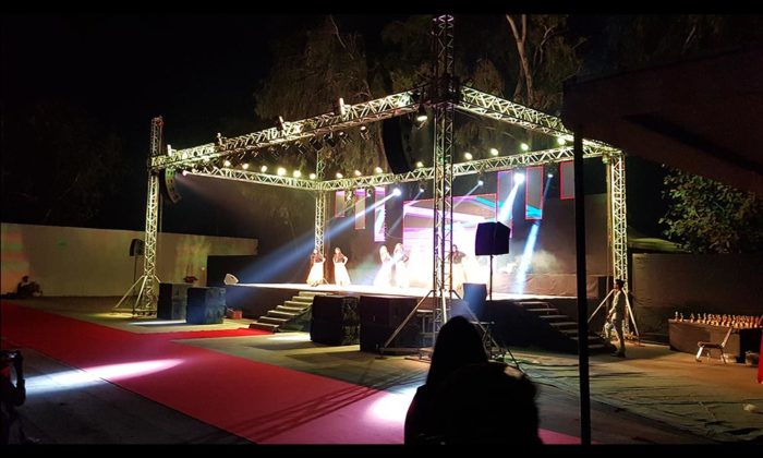 Dancers performing on the same open-air truss stage lit in white/blue, red carpet visible in the foreground.