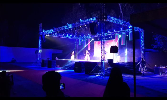 Performers dancing on the same open-air truss stage lit in blue, matching the backdrop graphic seen in the other photos of this stage.