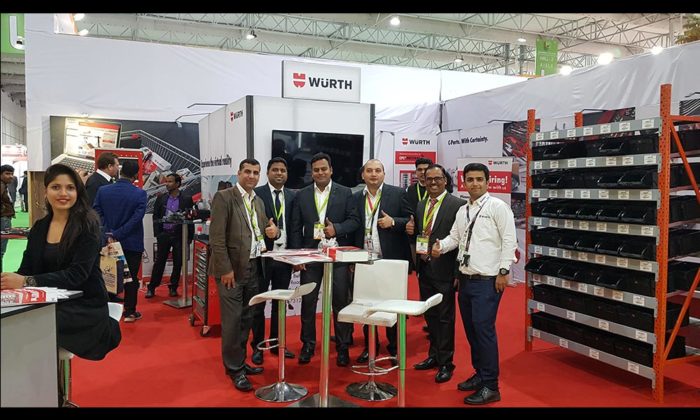 Group of staff giving thumbs-up at the same WÜRTH trade show booth, product shelving and signage visible behind.