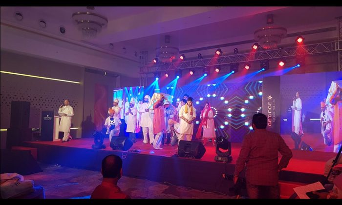Performers in white traditional attire on stage in front of a "GETINGE - Passion for Life" branded backdrop under blue lighting.