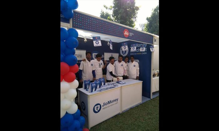 Staff posing at the same JioMoney exhibition booth, red-white-blue balloon decorations at the entrance.