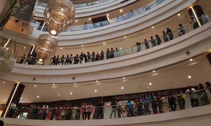 Overhead view of mall balcony levels crowded with onlookers beneath chandeliers, near a United Colors of Generation storefront; appears to be the audience watching the same mall event from above.