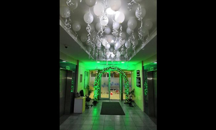 Office elevator lobby decorated with a green balloon arch and hanging white balloons for a celebration; no legible branding.