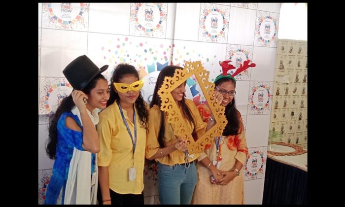 Group of women posing with photo-booth props (top hat, mask, antlers, frame) at the same Concentrix "Our Time Is Now" branded backdrop.